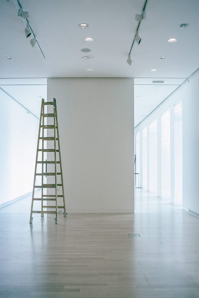 Foto eines weißen zweigeteilten Flurs mit großen Fenstern und Tageslicht in dem eine hohe Leiter steht