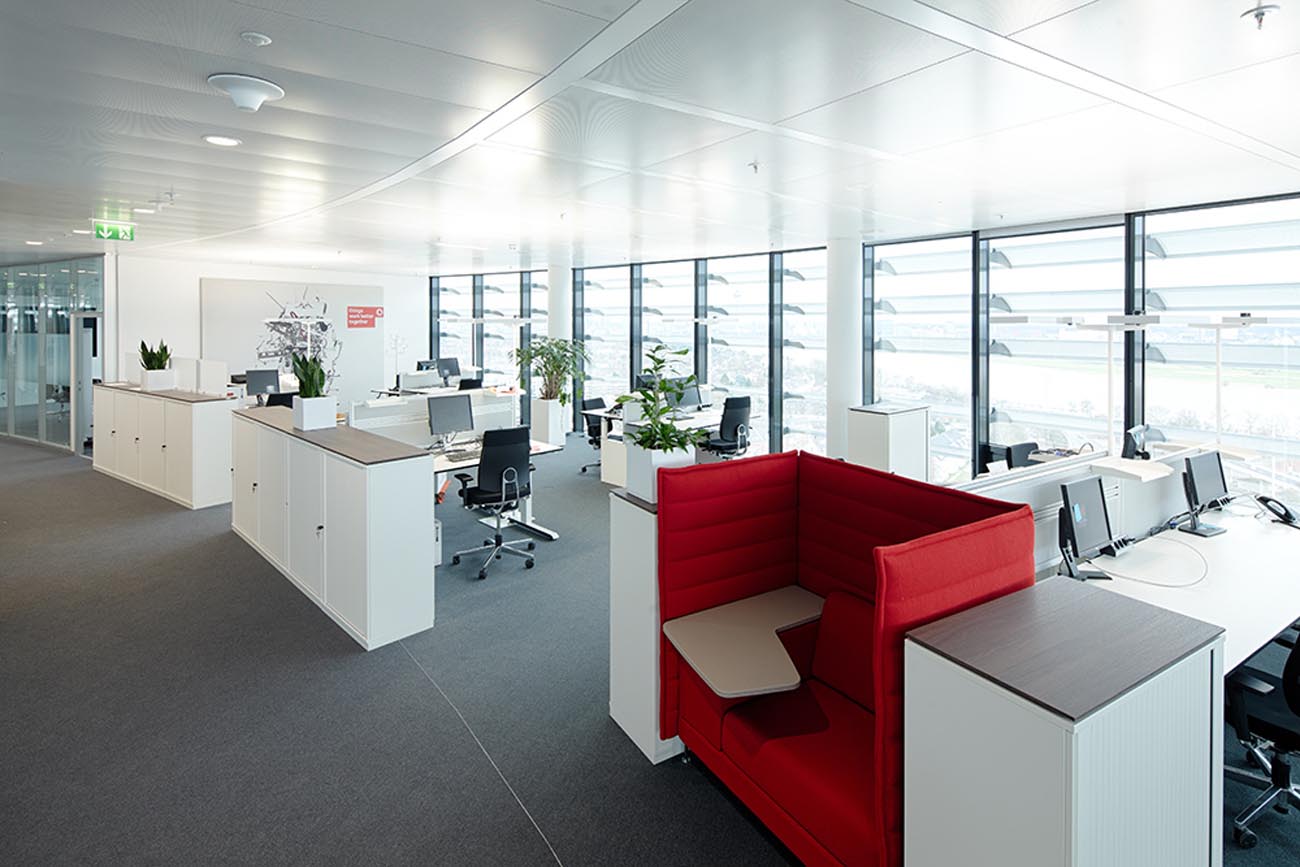 Offene Bürofläche mit vielen Arbeitsflächen und mittendrin ein rotes Sofa