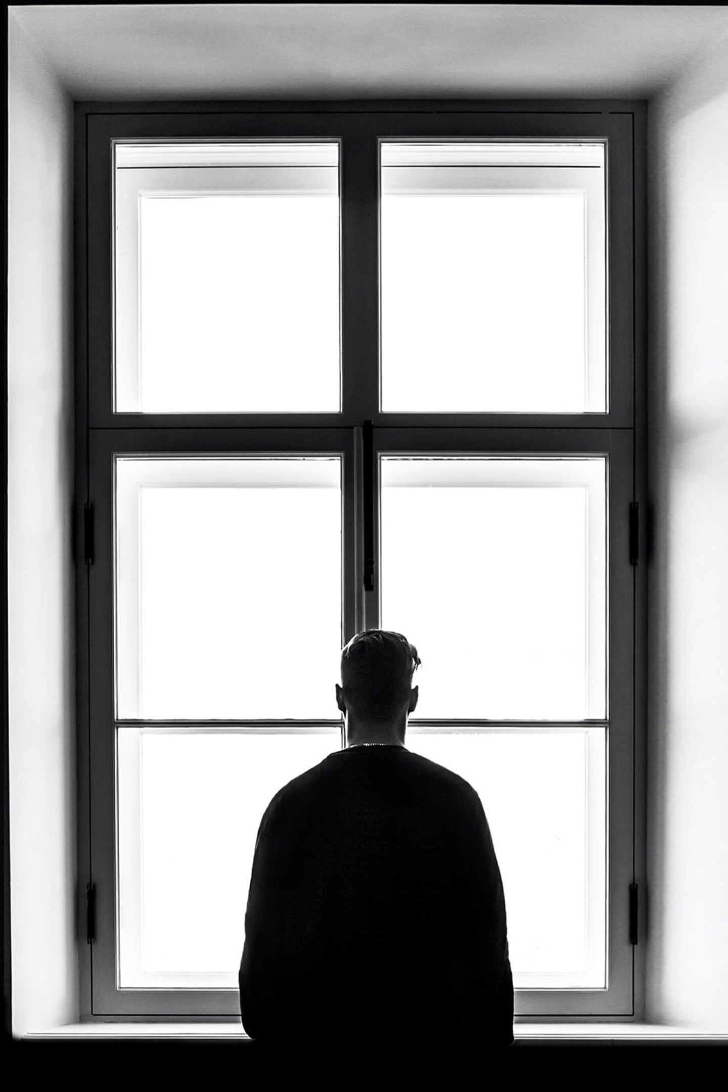 Schwarz-Weiß-Foto eines dunkel gekleideten Mannes, der vor einem großen Sprossenfenster steht