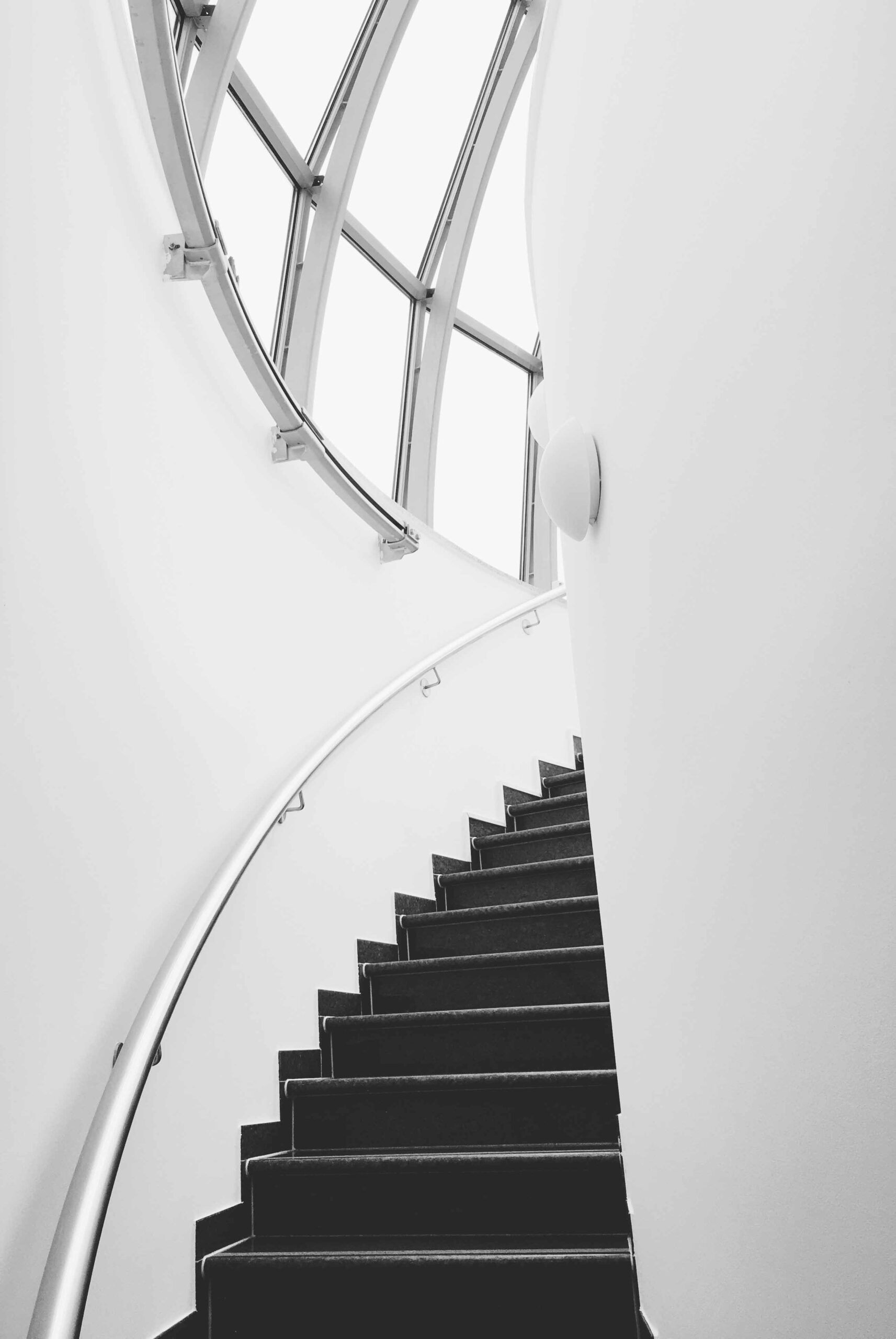 Eine rund geführte Treppe in einem weißen Turm führt zum gläsernen Dach