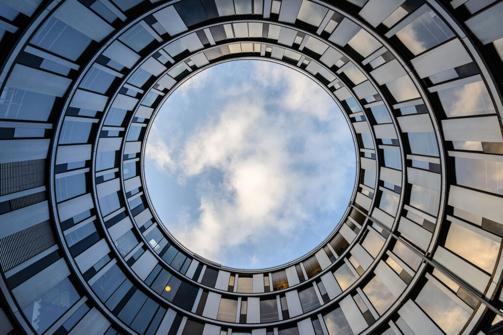 Aus einem Innenhof nach oben fotografiertes rundes Gebäude mit vielen Fenster und Blick in den Himmel
