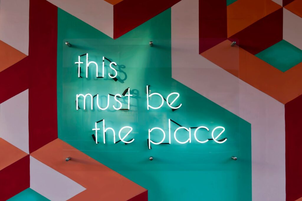 Auf einer bunten Wand mit vielen Formen hängt eine Leuchtschrift "This must be the Place"