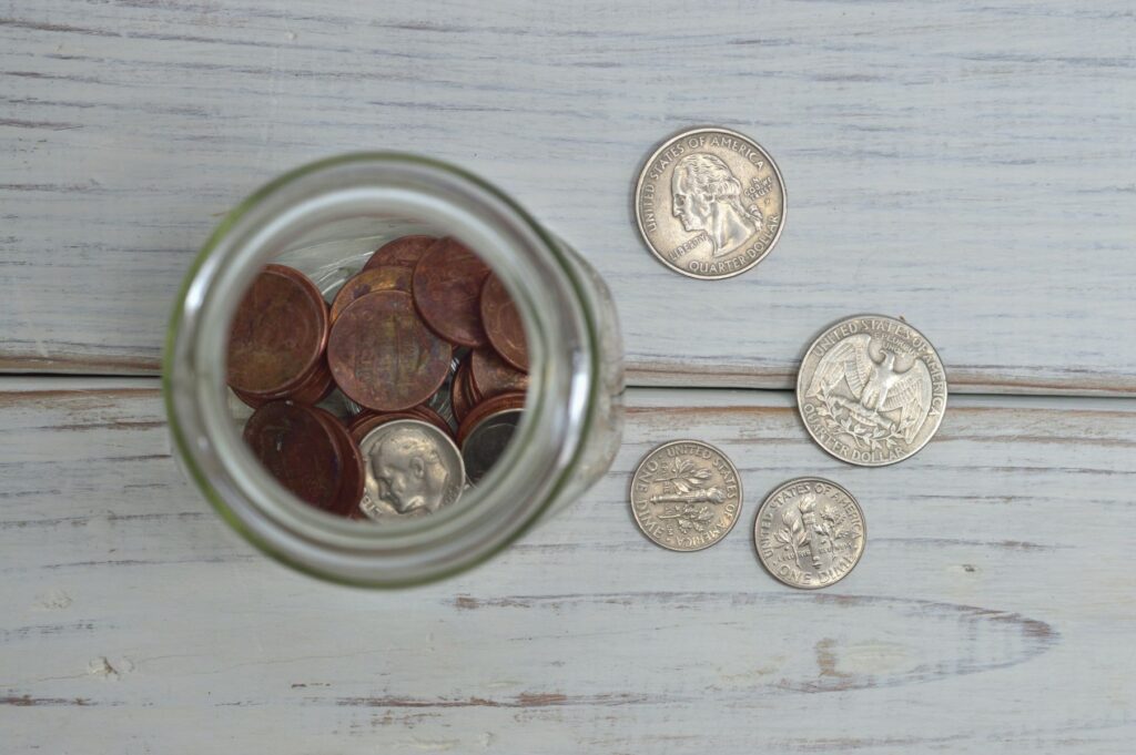 Auf einem weiß lasierten Holztisch steht ein Glas mit Cents Dimes und Quarter Dollars