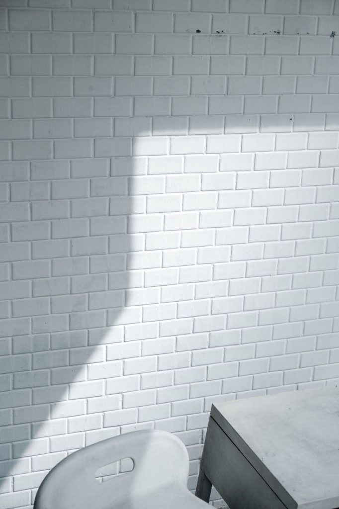Ausschnitt eines Fotos von einer weiß gefliesten Wand mit einem weißen Plastikstuhl und einem schmutzigen weißen Tisch