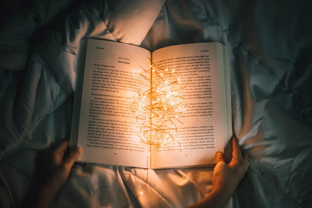 Auf einer Bettdecke liegt ein aufgeschlagenes Buch, in das eine kleine Lichterkette gewickelt ist