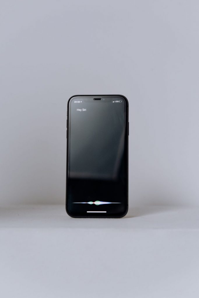 Foto eines schwarzen iPhones in einer weißen Hohlkehle auf dem Display ist der Kontakt zur Sprachassistentin Siri zu sehen