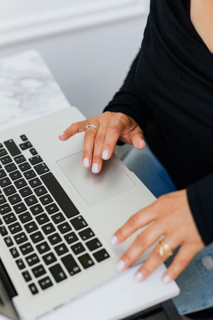 Fotoausschnitt mit einer Frau die an einem Marmortisch sitzt und auf ihrem MacBook tippt
