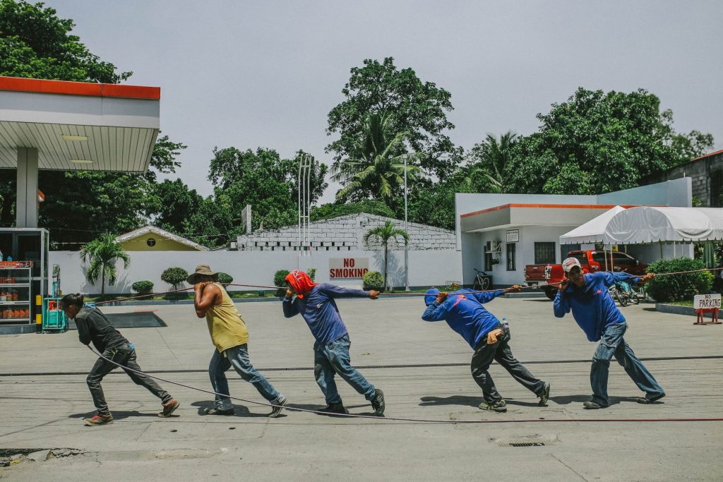 Auf einem Parkplatz zwischen Tankstelle und Hotel ziehen fünf Männer in Arbeitskleidung an einem Seil