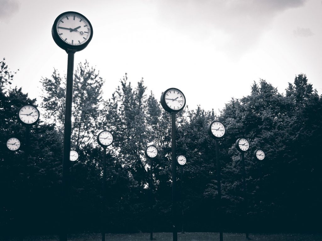 Ein schwarzweiß Foto zeigt viele Bahnhofsuhren mit der Uhrzeit viertel vor zwei in einem Park