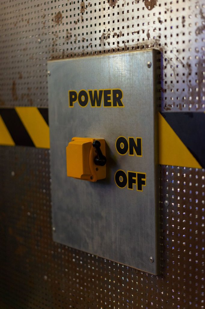 Auf einer Metalloberfläche mit Ausstanzungen befindet sich ein Schalterpanel mit einem großen gelben Schalter und den Wörtern POWER on off