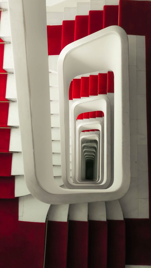 Blick von oben ein weißes Treppenhaus mit rotem Teppich hinab