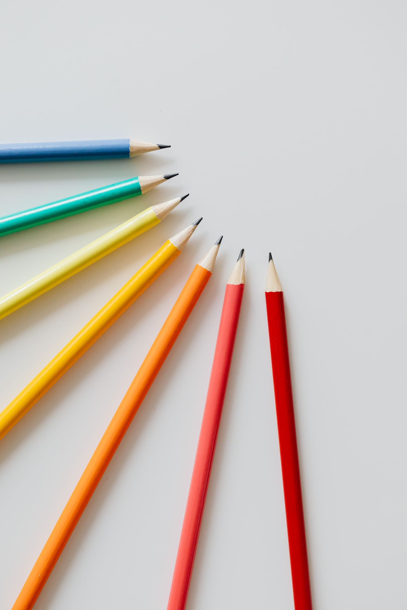 Vor einem weißen Hintergrund liegen Bleistifte in Regenbogenfarben