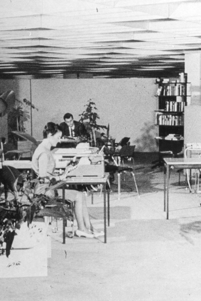 Unscharfes Schwarzweiß Foto von einer alten Bürosituation mit einer Frau an der Schreibmaschine und einem Mann am Schreibtisch