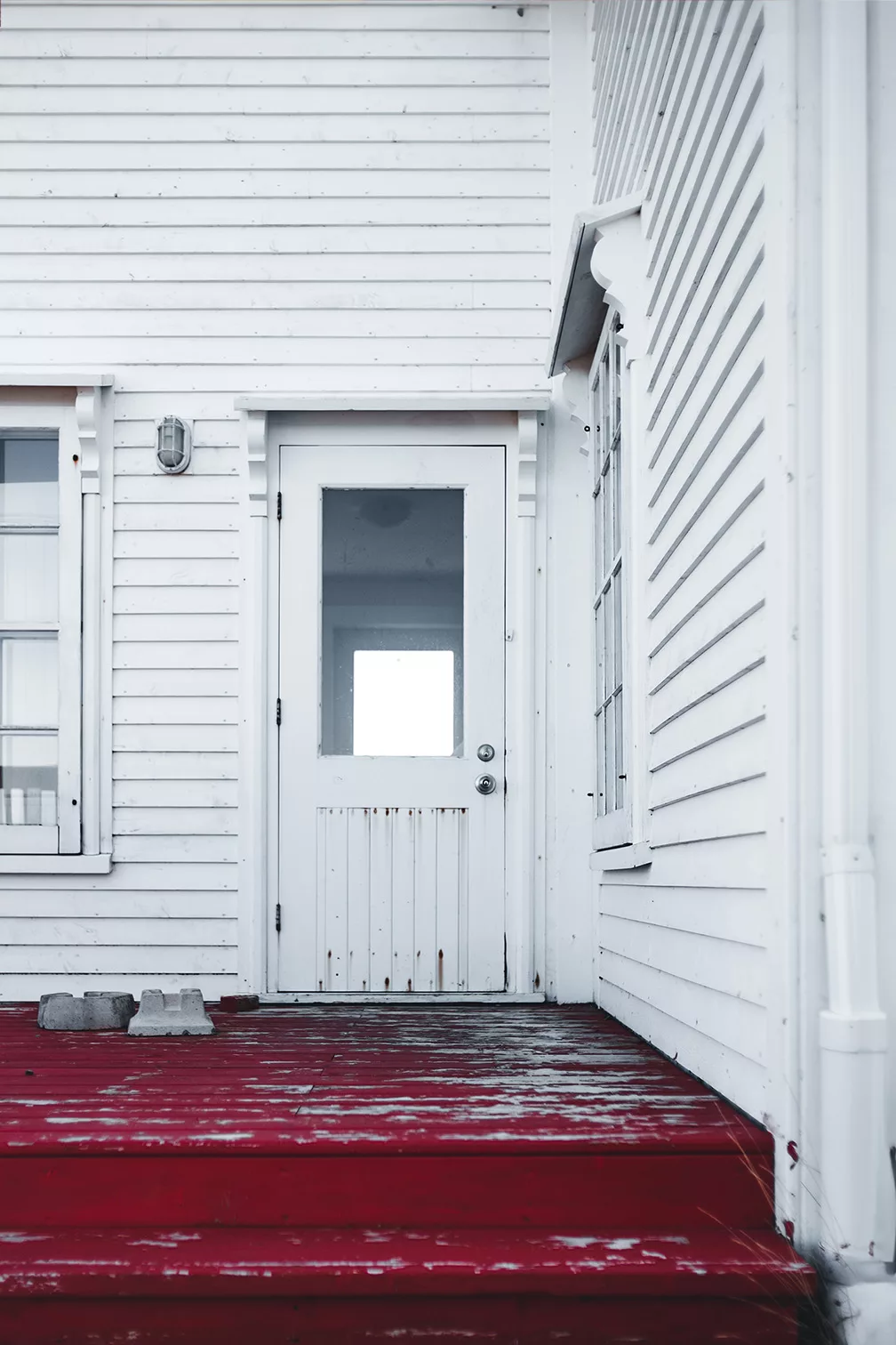 rot lackierte Holzstufen vor einem weiß gestrichenen Holzhaus mit Eingangstür