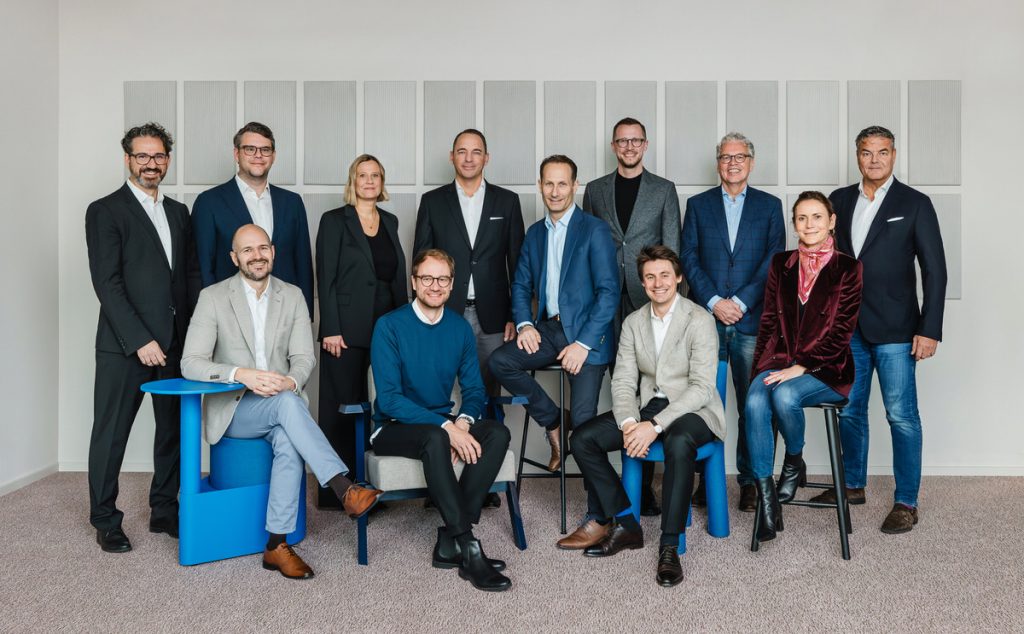 Eine Gruppe von Menschen steht vor einer Wand. Sie sind Business Casual gekleidet.